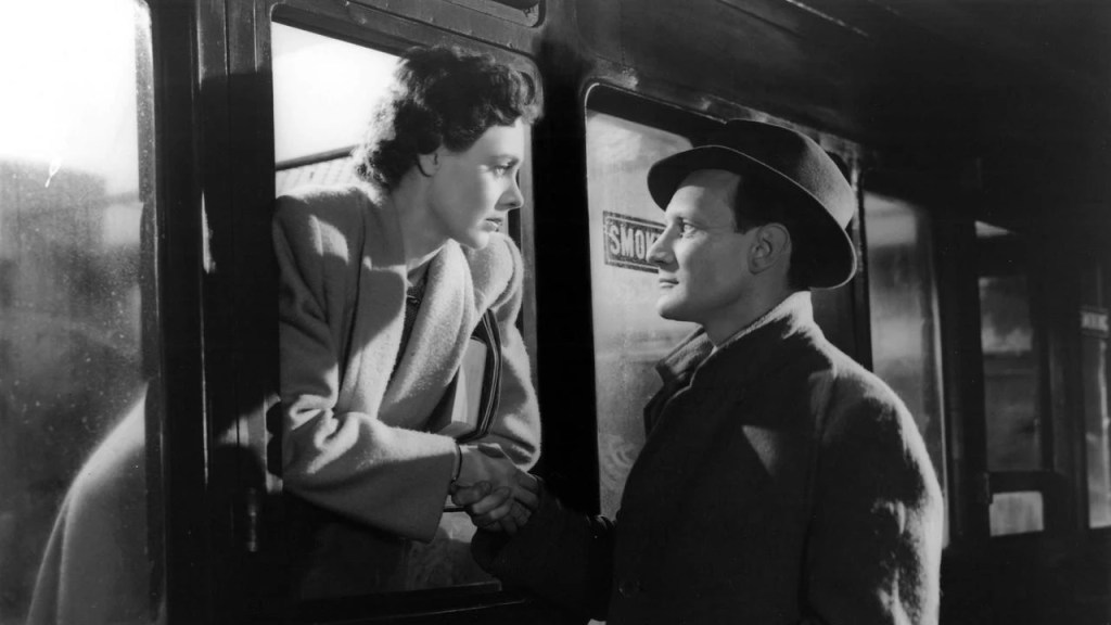 Una pareja se despide junto a un tren detenido. La escena, en blanco y negro, está cargada de tensión, deseo reprimido y despedida inevitable.
(Brief Encounter, David Lean, 1945)