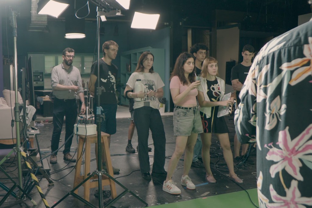 Escena de la película Orgullo y prejuicio de Matías Szulanski donde los actores aparecen en una toma diagonal a la cámara, interactuando en un set que simula una obra de teatro con artificialidad corpórea.